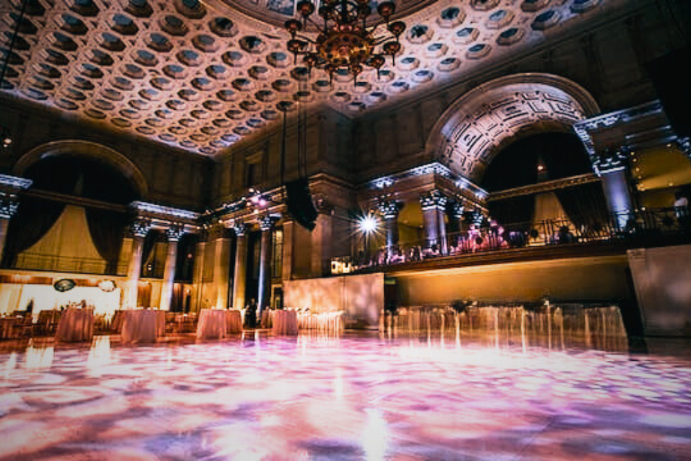 An Israeli wedding band and singers perform in the grand Cipriani New York ballroom, with a 12-piece orchestra and DJ hybrid setup providing live music under a high coffered ceiling.